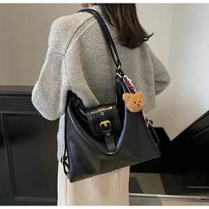 Detail of black faux leather hobo bag with gold buckle and teddy bear charm on shoulder