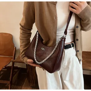 Detail of dark brown hobo bag with silver chain and leather strap in an indoor setting
