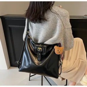 Detail of black glossy leather tote bag with gold buckle and brown plush bear charm