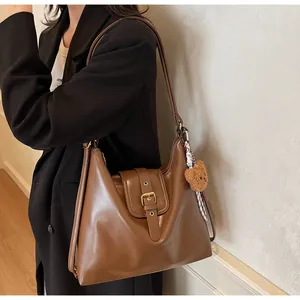 Detail of caramel brown leather tote bag with gold buckle and cute bear charm pendant