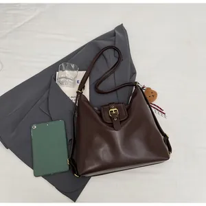 Detail of dark brown leather shoulder bag with gold buckle and cute bear pendant charm