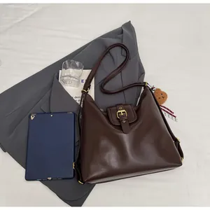 Detail of a brown large-capacity shoulder bag with a gold buckle and plush bear charm