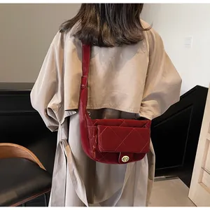 Close-up of deep red quilted crossbody bag with golden metal twist lock on camel coat