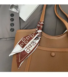 Detail of brown litchi grain leather tote bag with elegant floral scarf on handle