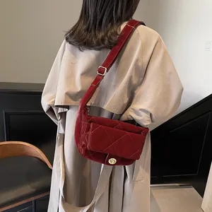 Deep red quilted patent leather saddle bag with golden clasp worn on a khaki coat