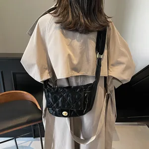 Quilted black crescent crossbody bag with gold buckle on a beige trench coat