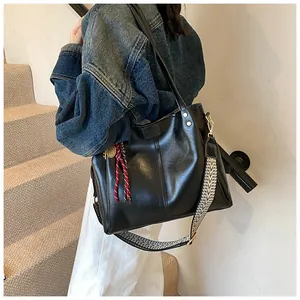 Dettaglio borsa tote in pelle nera con tracolla geometrica indossata da modella su scale
