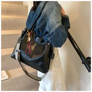Dettaglio borsa tote in ecopelle nera con tracolla larga e ciondolo con frange