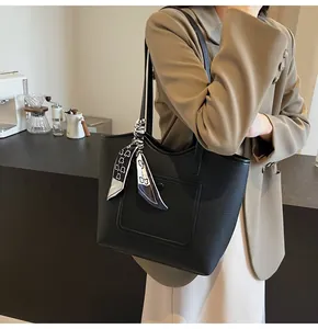 Detail of black pebbled leather tote bag featuring a printed silk scarf on the handle