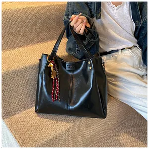 Dettaglio borsa tote in pelle nera con pendente a corda rossa e texture raffinata