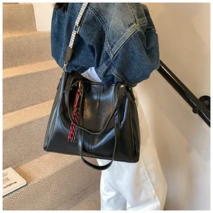 Dettaglio borsa tote in pelle nera con tracolla geometrica e nappa rossa decorativa
