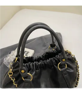 Close-up of black pleated PU handbag with soft cylindrical handles and gold hardware