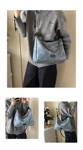 Close-up of washed blue denim hobo bag with bronze chain and adjustable black strap