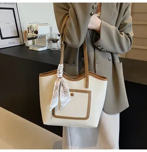 Detail of a beige tote bag with brown trim and a decorative printed silk scarf on handle