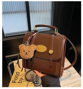 Détail du sac à main marron avec plaque logo dorée et charm d'ours en peluche