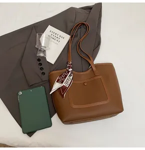 Brown lychee leather tote bag with a decorative wine red silk scarf on soft white bedding
