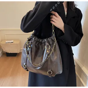 Detail of dark brown vintage faux leather handbag with elegant pleats and gold chain accents