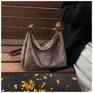 Close-up of retro mocha suede tote bag with metal chain and strap on autumn leaves