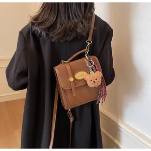 Détail du sac à main en cuir marron avec pendentif ours et ruban à carreaux