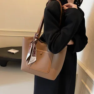 Brown lychee leather tote bag with printed bear scarf on handle, worn with black coat