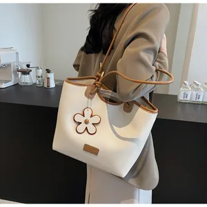 Detail of cream tote bag with brown trim featuring a floral charm and knotted handles