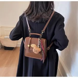 Sac à dos vintage en cuir marron avec plaque logo dorée et breloque ours en peluche