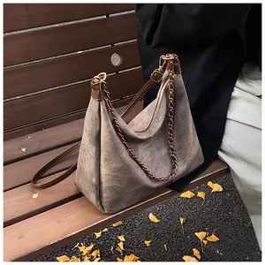 Close-up of retro suede tote bag with metal chain detail on a park bench with autumn leaves