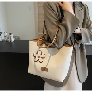 Detail of a beige pebbled leather tote bag with brown straps and a floral charm