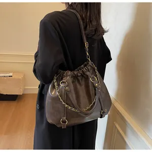 Detail of a dark brown pleated cloud bag with gold chain and crossbody strap shown on a model