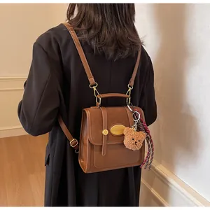 Détail d'un sac à dos vintage en cuir marron avec plaque dorée et pendentif ours