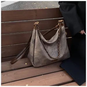 Detail of taupe suede tote bag with brown straps and metal chain on a wooden bench