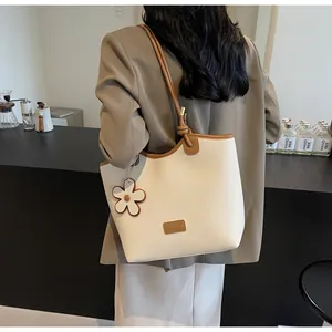 Chic cream bucket bag with brown trim and flower charm shown on a fashion model
