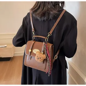 Détail d'un sac à dos vintage marron avec breloque ours en peluche et pompon tissé