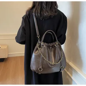 Macro detail of dark brown pleated tote bag with drawstring closure and gold chain