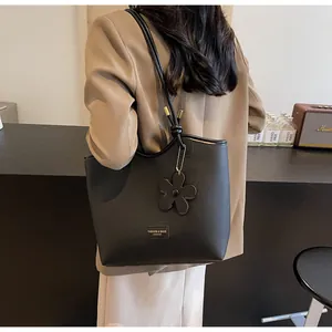 Close-up of black litchi grain leather tote bag with floral charm and gold logo detail