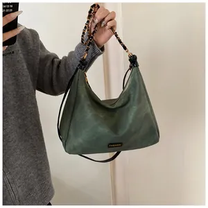 Close-up of retro dark green suede tote with woven metal chain and fashion plaque