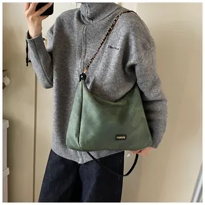 Detail of dark green faux suede shoulder bag with chain strap on grey knit sweater