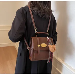Détail d'un sac à dos en cuir marron avec poignée dorée et ruban décoratif à carreaux
