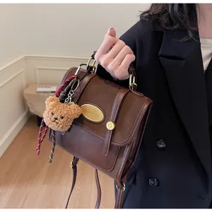 Détail d'un sac à dos vintage en cuir marron avec logo doré et charm d'ours