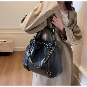 Detail of black pleated faux leather handbag with gold chain and top round handle