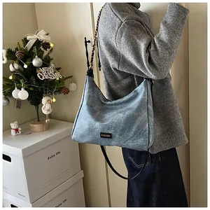 Detail of light blue washed denim hobo bag with braided chain strap and leather logo