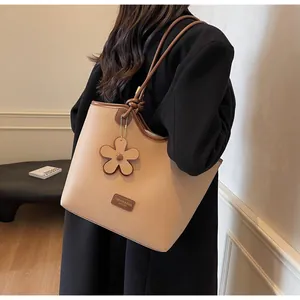 Detail of beige lychee leather bucket bag with brown handles and flower charm pendant