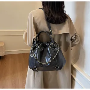 Detail of black pleated PU leather crossbody bag with gold chain on a model in trench coat