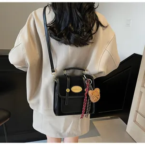 Détail d'un sac bandoulière rétro en cuir noir avec breloque ours et foulard en soie