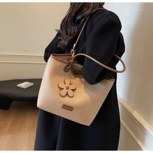 Detail of minimalist cream bucket bag with brown trim and floral charm on black coat