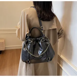 Black pleated PU leather tote bag with gold chain strap detail on a trench coat model