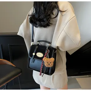 Détail d'un sac à main noir en cuir PU avec emblème doré et breloque ours en peluche