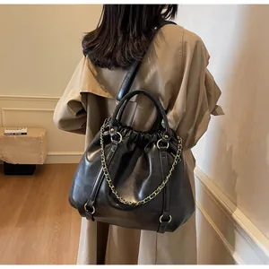 Detail of a black pleated leather tote bag with gold chain strap on a khaki trench coat