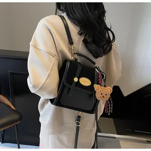 Détail d'un sac à main noir en cuir avec boucle dorée et breloque ours en peluche