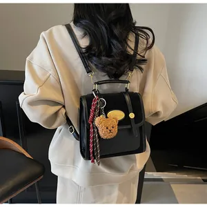 Détail du sac à dos en cuir noir avec plaque dorée et breloque ours en peluche marron